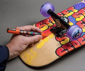 En person som tegner på ett skateboard med POSCA tusjer