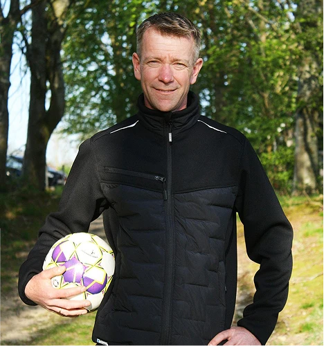 En mann i en svart jakke med en fotball under armen