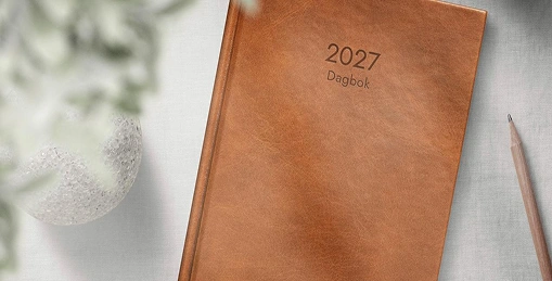 En brun kalenderbok for 2027 med en blyant ved siden av
